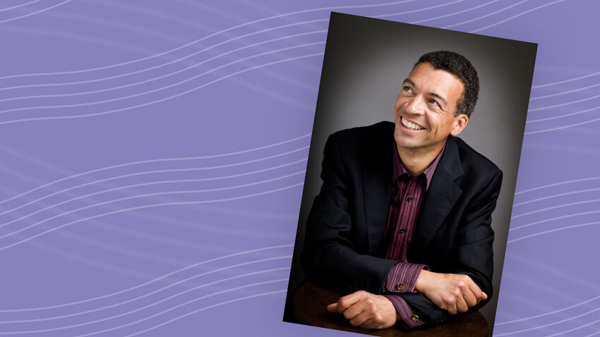 Roderick Williams headshot, wearing a black blazer, with a grey background, smiling with his head turned slightly to the left