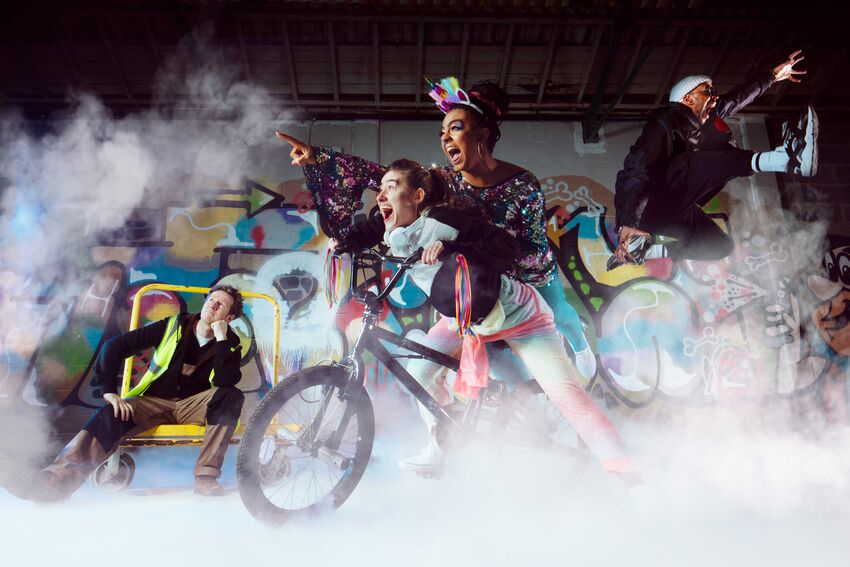 Two people are on a BMX bike, looking and pointing to the left, behind them a person sits looking pensive and another is jumping, arm outstretched