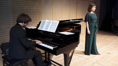 Man playing piano and woman in green dress singing