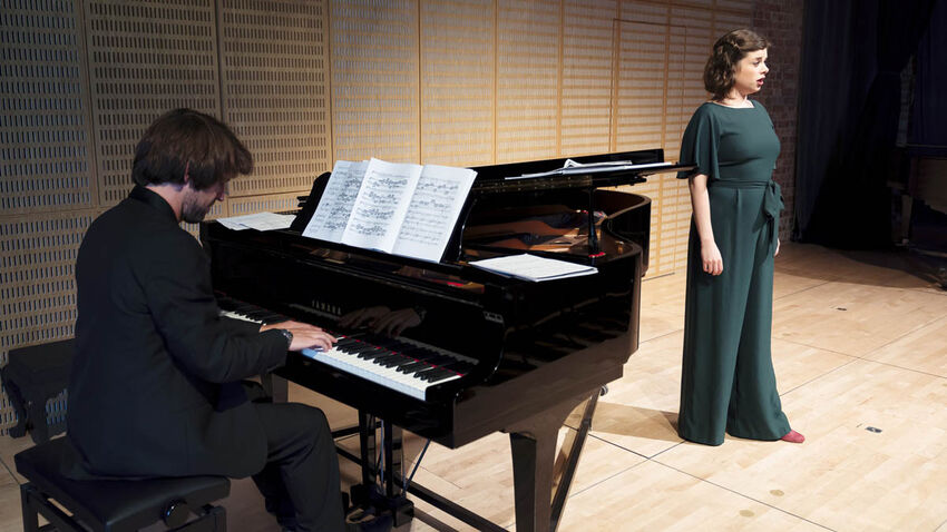 Man playing piano and woman in green dress singing