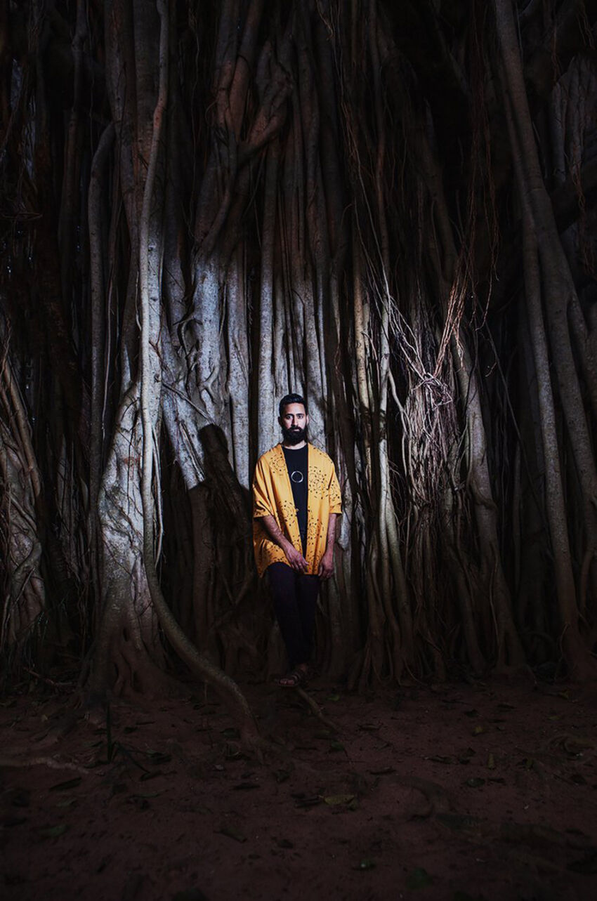 Sarathy Korwar waers all black with an orange jacket, surrounded by dark atmospheric trees