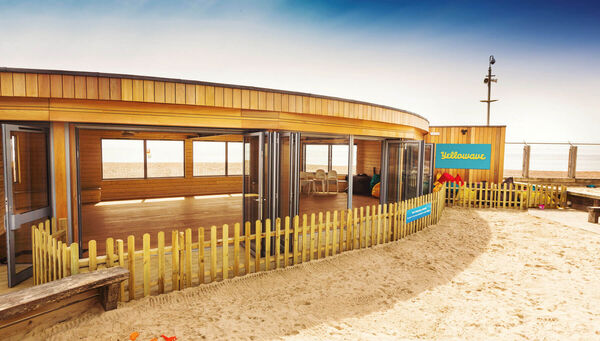 Yellowave Beach House, a single story wooden building with large open windows and sand in front of it