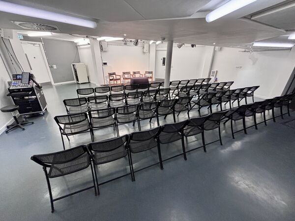 A white room with grey floors and black chairs laid out in rows facing the front