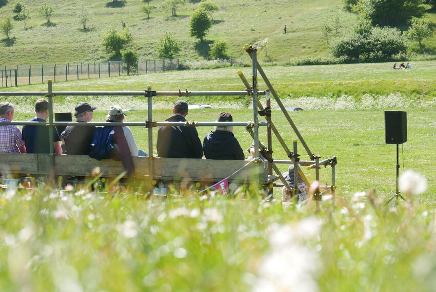 Bleechers made out of scaffolding sit amongst a green field