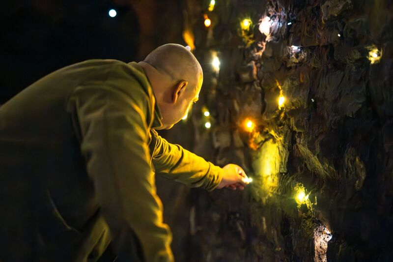 A man leans down to place a small light onto a cave wall with other lights