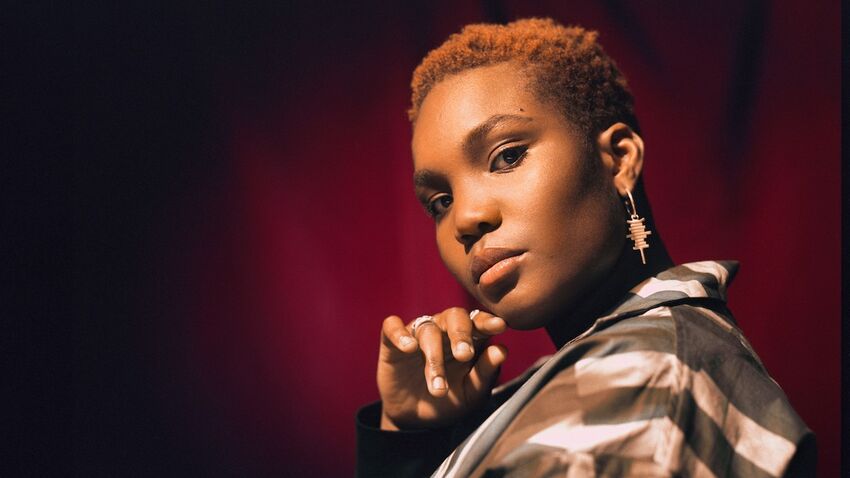 Arlo Parks holds her hand under her chin in front of a dark red curtain