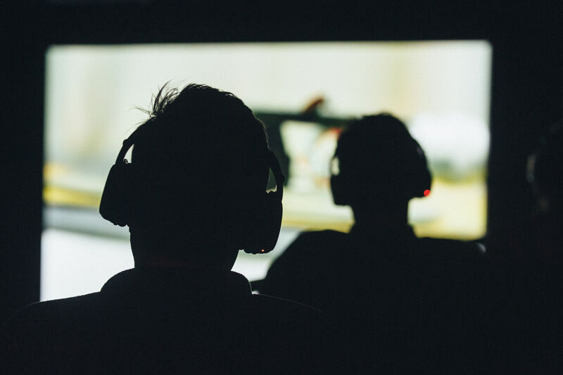 Silhouettes against a large video of two people wearing headphones
