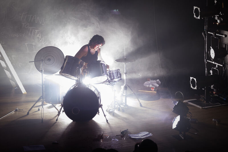 On stage picture of a performer drumming, illuminated from the back by a powerful white light