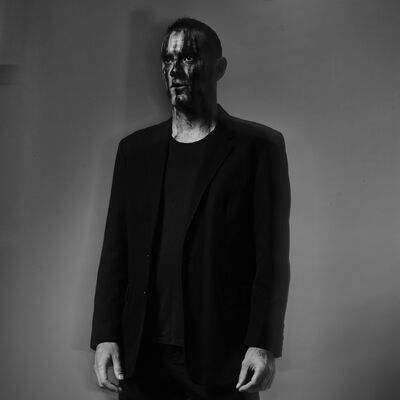 A man in an all-black outfit, with black paint smeared over his face