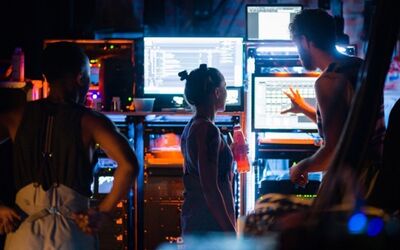 A person shows two people several computer monitors and mix desks