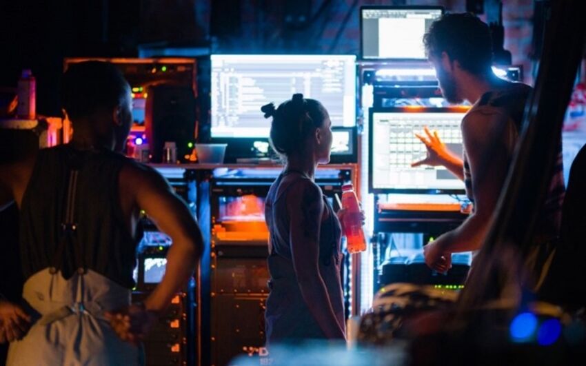 A person shows two people several computer monitors and mix desks