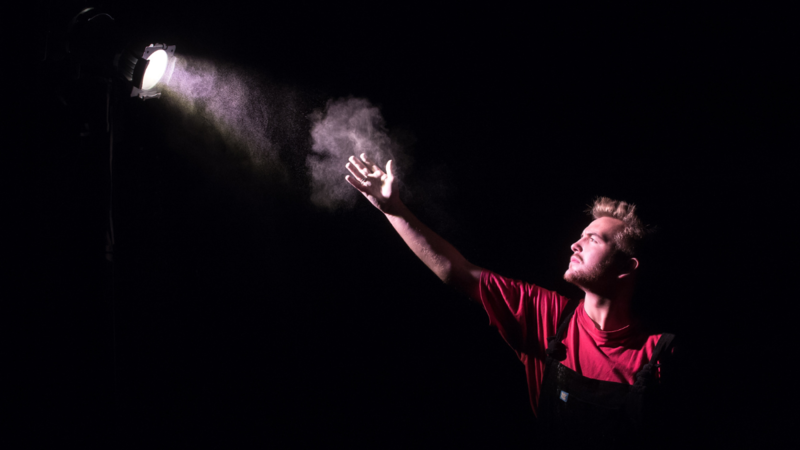 A person in a red top, reaching up to a white beam of light