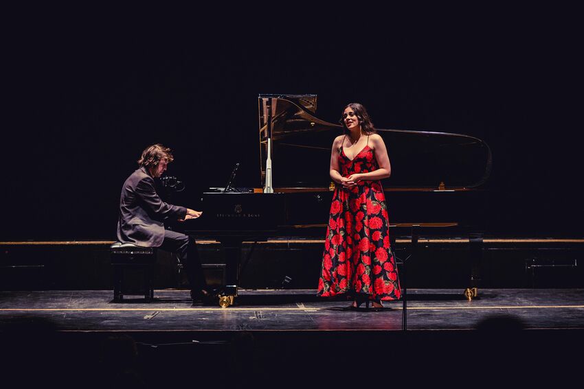 Jerwood Youngs Artists event from 2021 - a man in a black suit plays piano on stage, with a woman waring a long black dress with red flowers sings at the front of the stage