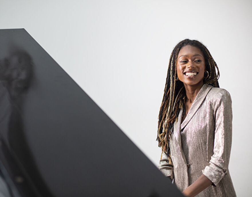 Isata Kanneh Mason stands smiling behind a grand piano