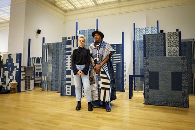 A man and a woman stand in front of there large artworks