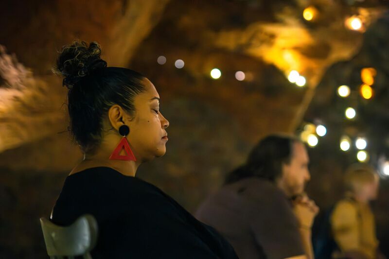 A woman sits calmly in a chair with her eyes closed, a cave of small lights behind