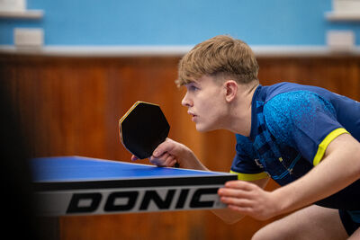 A young man is playing table tennis. He is poised mid-game with his bat
