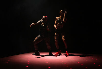 Two performers stand dancing in the middle of a dimly lit stage
