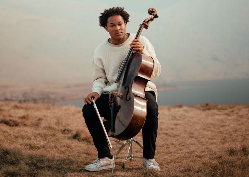 Sheku Kanneh-Mason sits outside holding a cello