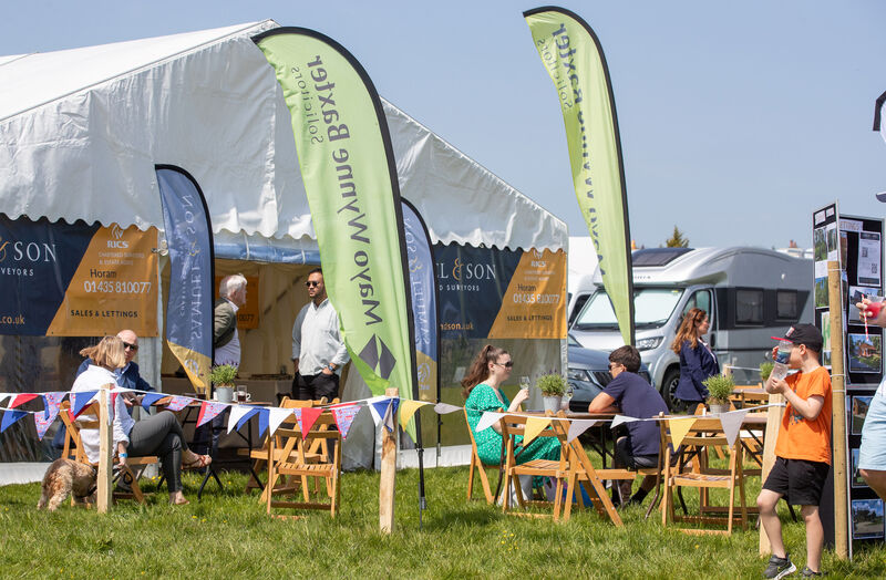 An event tent on grass with wooden fold up chairs and feather banners outside of it