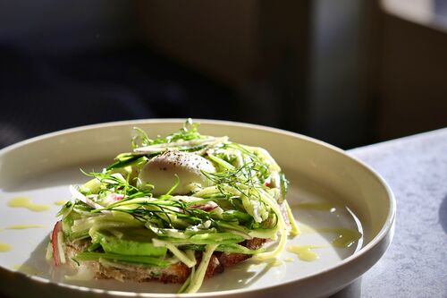 A plate of food, lots of green vegetables on top of a potato rosti with a poached egg in the middle