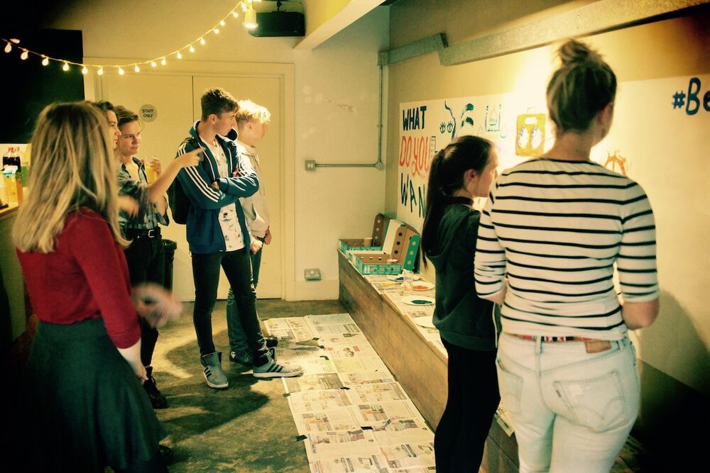 A group of young people are gathered in a studio space. They are looking at a visual art display