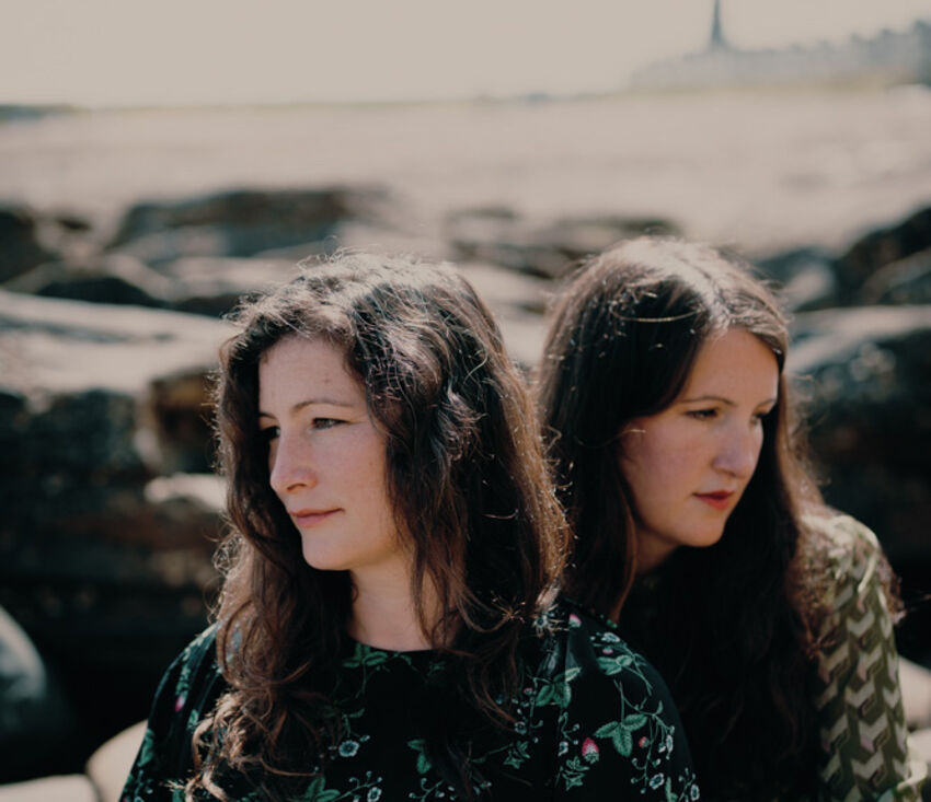 Two people are sat close together, one looking off to the left and the other to the right