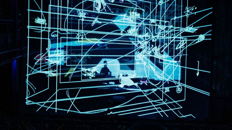 Max Cooper DJing with layers of blue squares projected over him