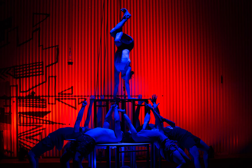 The Out of Chaos acrobats form a human tower, highlighted in blue against a red background.