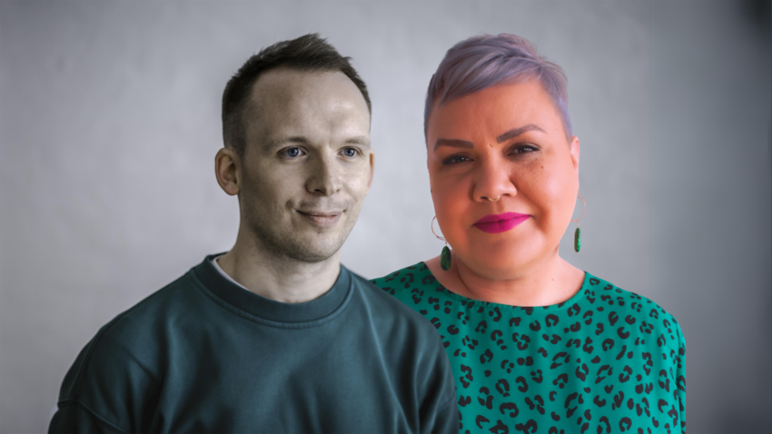 A white man in with short hair wearing a greenish jumper stands next to a woman with short grey hair and a green leopard print top