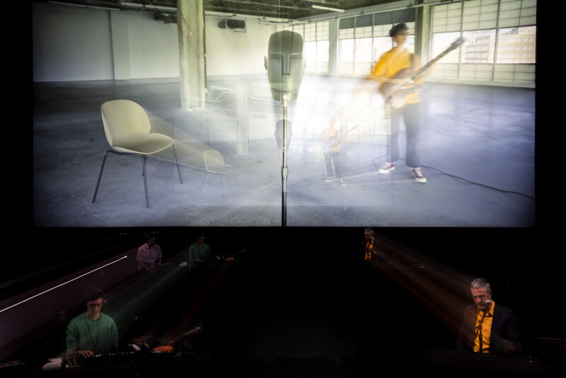 A large screen with a video mid-transition of a person playing guitar in an empty room and a close-up of a microphone