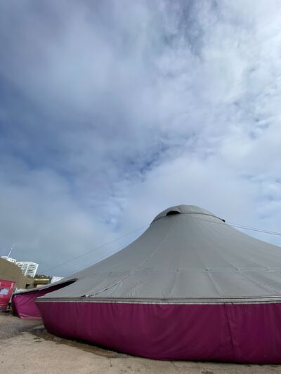 A silver and pink big top tent, on concrete floor, with a cloudy blue sky above.