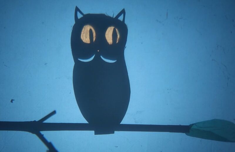 A paper puppet owl sits backlit on a branch