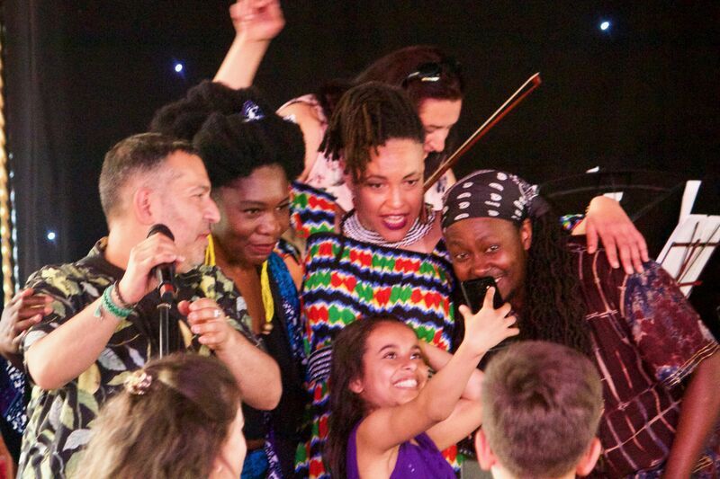 Four musicians from One World Orchestra pose behind a young girl holding her phone up to take a selfie with them