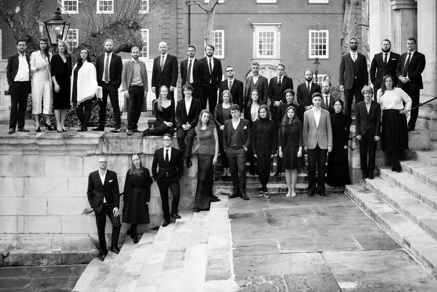A grayscale photo of 33 people in smart clothes pose standing on steps and a short wall behind