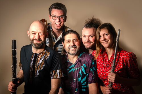 A group of 5 musicians in colourful shirts. Two of them are holding flutes/clarinets
