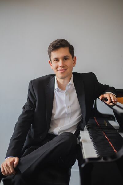 Jamie Cochrane wearing a black suit and white shirt sat at a piano