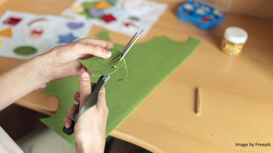 Hands holding scissors to cut out a leaf shape from green felt