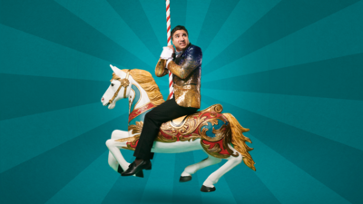 A man looking concerns wearing a blue and gold sparkly blazer sitting on a carousel horse
