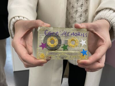 A cassette tape is held towards the camera. It is glittery and covered in star shaped stickers with the words 