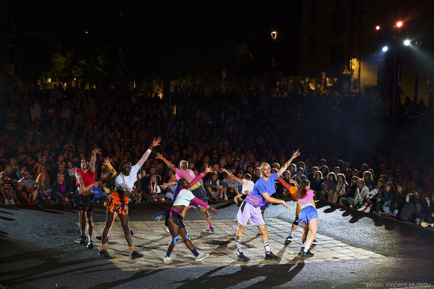 A large group of performers wearing colourful clothes performing in a huge outdoor space