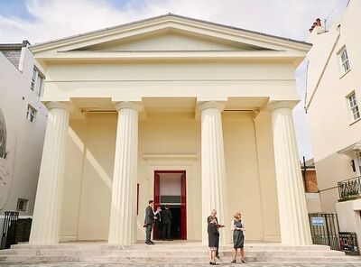 The front of a large white building with a pointy roof and four large pillars at the front