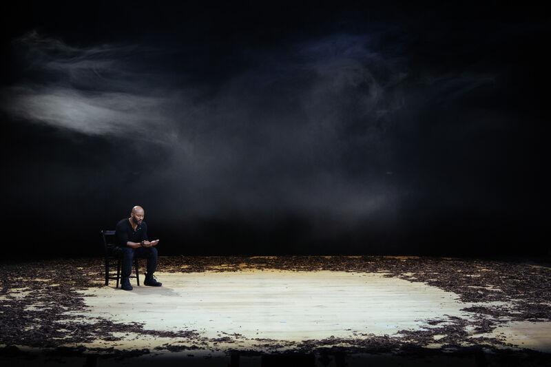 Man sitting on a stage with debris. He is sitting on a chair with haze around him