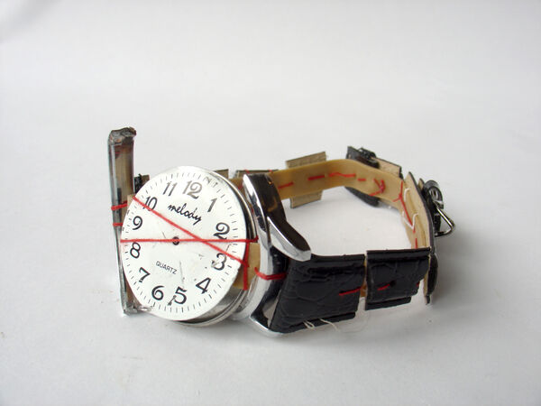 A broken wristwatch with a black strap, sowed back together with a red thread