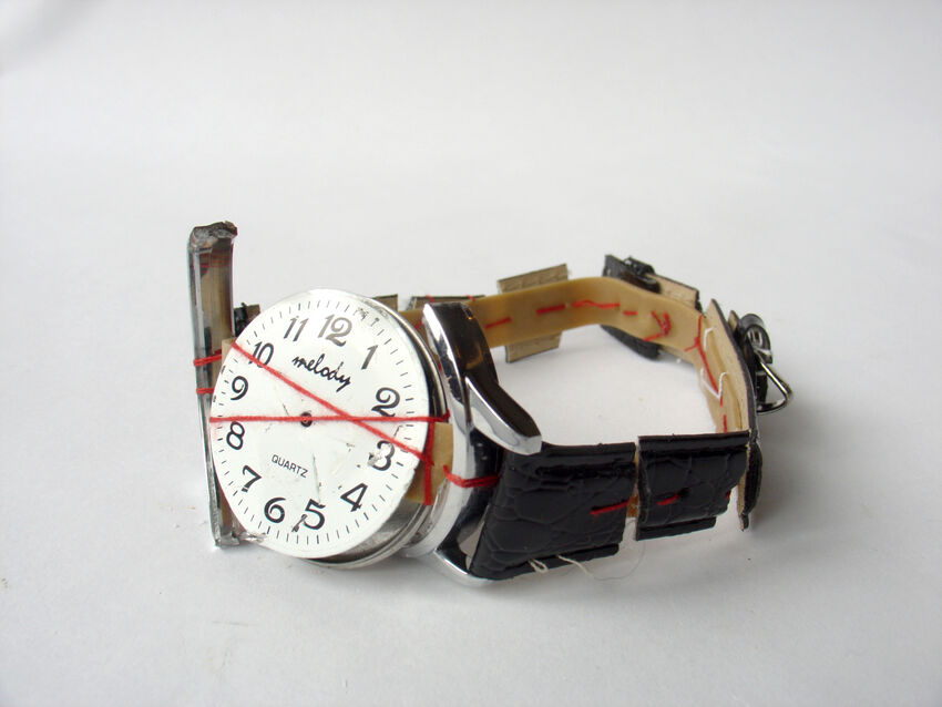 A broken wristwatch with a black strap, sowed back together with a red thread