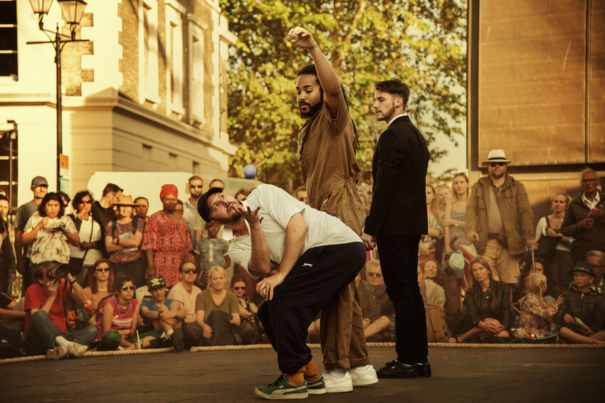 Three performers perform a trick with a small blue ball to a crowd
