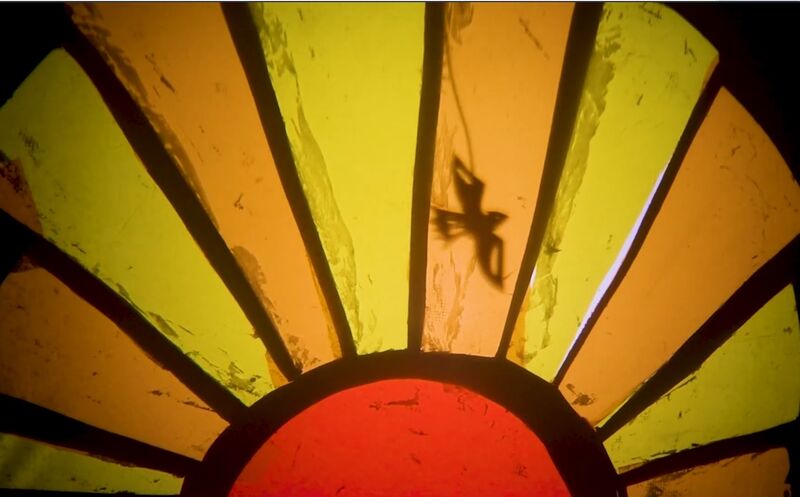 A paper puppet bird flies backlit across a paper sun