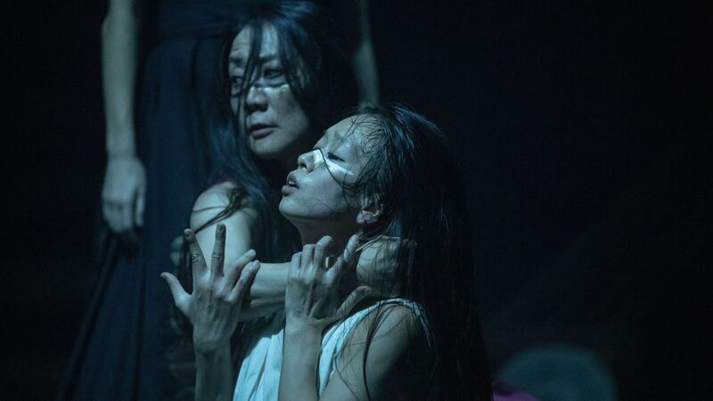 A girl stands sideways on with her hands raised up and her eyes closed. An older lady has her arm around the girl's neck