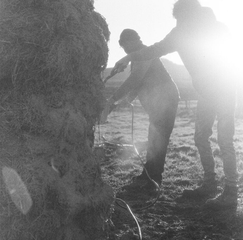 Material testing and scouting for the sculpture, two figures stand in front of a small hill with machines hooked into the soil