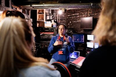 A woman standing backstage at a theatre talks to a group of people